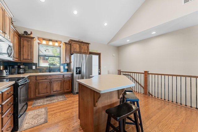 kitchen featuring lofted ceiling, light hardwood / wood-style flooring, appliances with stainless steel finishes, a center island, and a kitchen bar