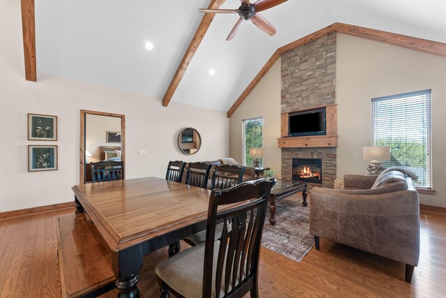 dining space featuring ceiling fan, a stone fireplace, hardwood / wood-style flooring, and high vaulted ceiling