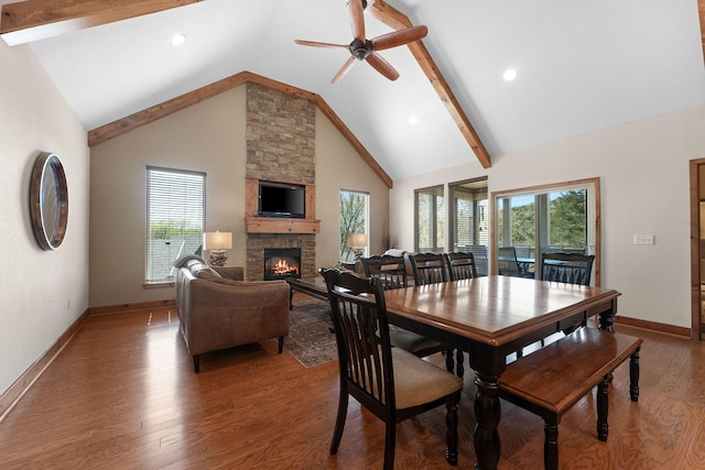 dining space with high vaulted ceiling, ceiling fan, hardwood / wood-style floors, a stone fireplace, and beam ceiling