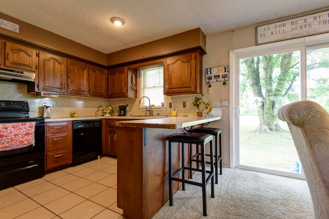 kitchen featuring a breakfast bar area, range hood, sink, kitchen peninsula, and black appliances