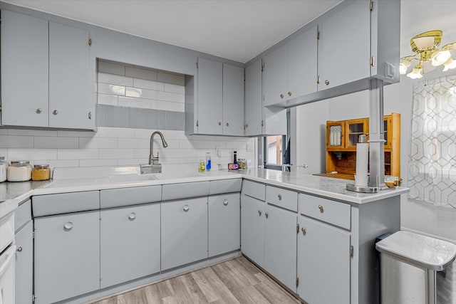 kitchen featuring decorative backsplash, sink, kitchen peninsula, light hardwood / wood-style flooring, and gray cabinets