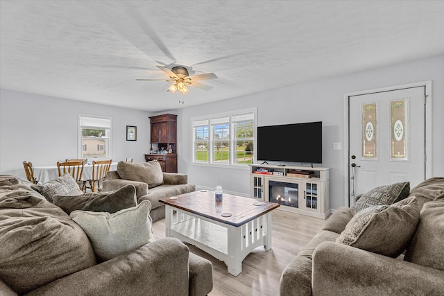 living room featuring ceiling fan, a textured ceiling, light hardwood / wood-style flooring, and a healthy amount of sunlight