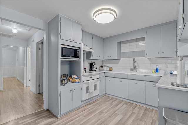 kitchen featuring gray cabinetry, light wood-type flooring, tasteful backsplash, white oven, and stainless steel microwave