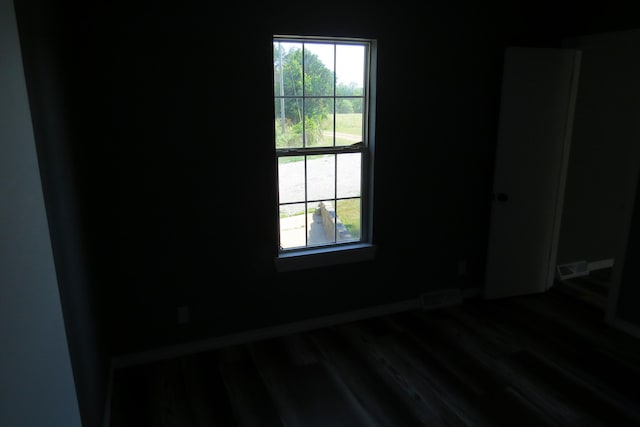 unfurnished room with wood finished floors, a wealth of natural light, baseboards, and visible vents