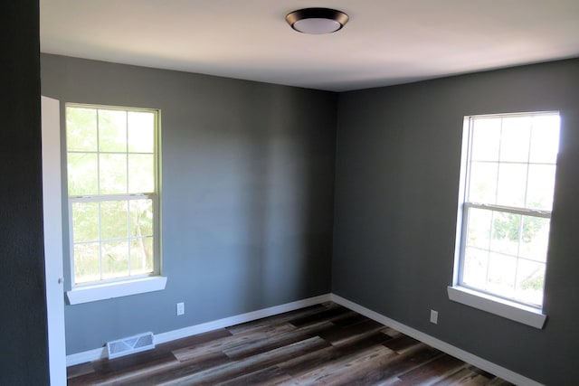 empty room with dark wood-style floors, baseboards, visible vents, and plenty of natural light