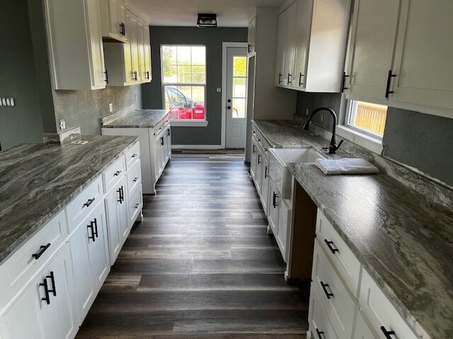 kitchen featuring tasteful backsplash, dark stone countertops, dark wood-type flooring, sink, and white cabinetry