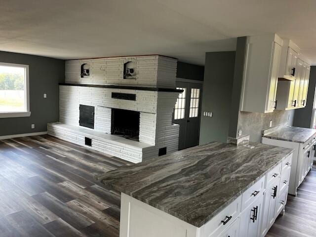 kitchen featuring white cabinets, stone countertops, a fireplace, dark wood finished floors, and baseboards