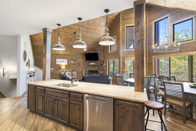 kitchen featuring pendant lighting, sink, wooden walls, high vaulted ceiling, and dishwasher