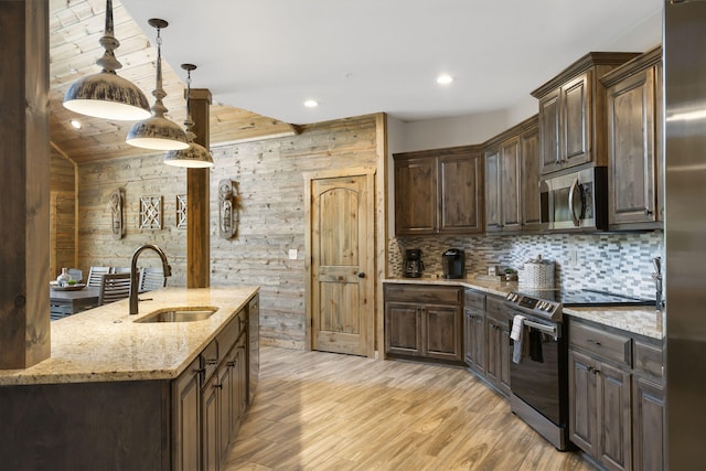 kitchen featuring pendant lighting, sink, wooden walls, light hardwood / wood-style flooring, and stainless steel appliances