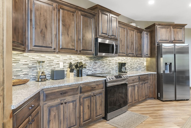 kitchen featuring light hardwood / wood-style floors, dark brown cabinets, light stone countertops, backsplash, and appliances with stainless steel finishes