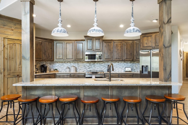 kitchen with pendant lighting, light stone countertops, appliances with stainless steel finishes, and hardwood / wood-style flooring