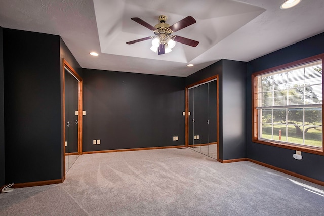 unfurnished bedroom featuring ceiling fan, a tray ceiling, and light colored carpet