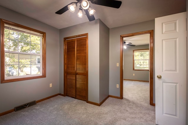 unfurnished bedroom featuring ceiling fan, a closet, light carpet, and multiple windows