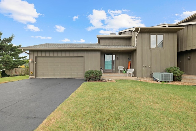 view of front facade with a front lawn, cooling unit, an attached garage, board and batten siding, and aphalt driveway
