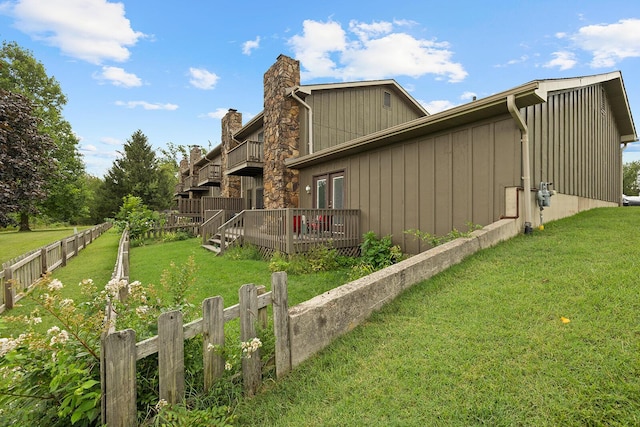 view of property exterior with a chimney, fence, a balcony, a yard, and a wooden deck