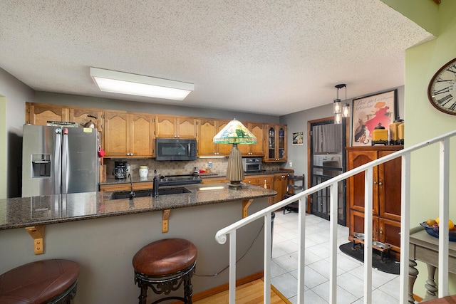 kitchen with a sink, backsplash, glass insert cabinets, brown cabinetry, and stainless steel refrigerator with ice dispenser