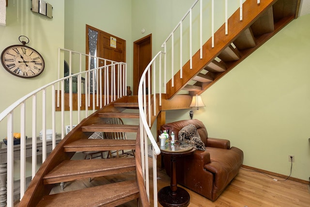 stairs featuring baseboards, a towering ceiling, and wood finished floors