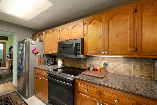 kitchen with a textured ceiling, light hardwood / wood-style flooring, appliances with stainless steel finishes, dark stone counters, and decorative backsplash