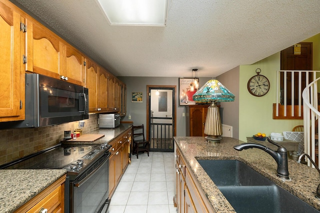 kitchen featuring a sink, brown cabinetry, black appliances, decorative backsplash, and light tile patterned flooring