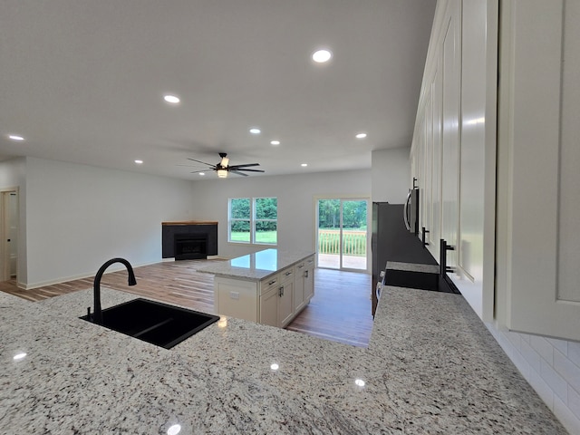 kitchen with light stone counters, ceiling fan, white cabinets, sink, and light hardwood / wood-style flooring