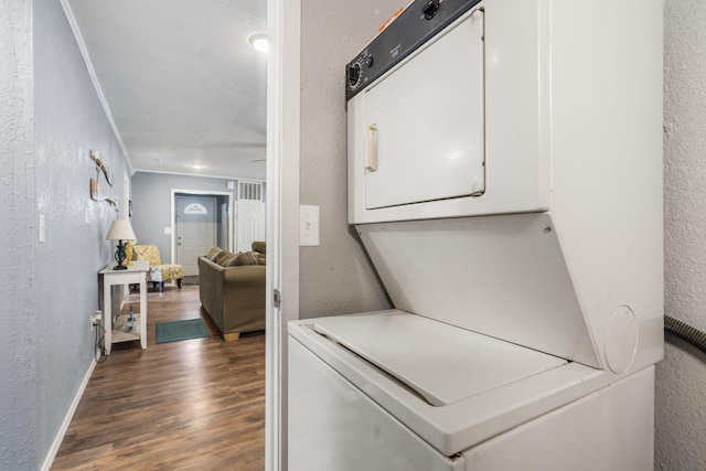 laundry area with dark wood-type flooring, ornamental molding, and stacked washing maching and dryer