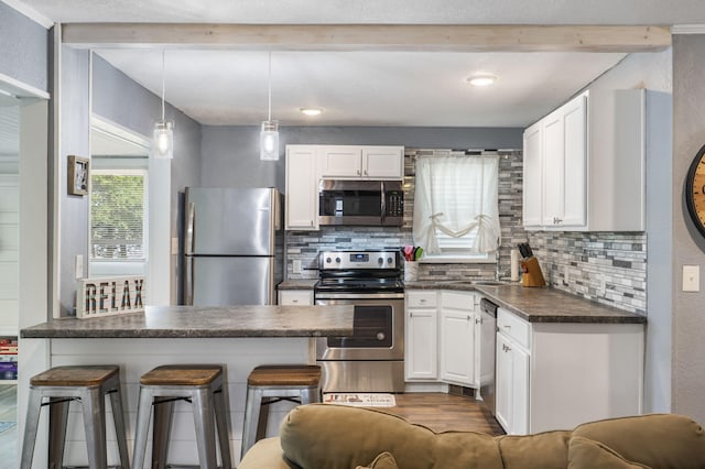 kitchen featuring pendant lighting, appliances with stainless steel finishes, backsplash, white cabinets, and a kitchen bar