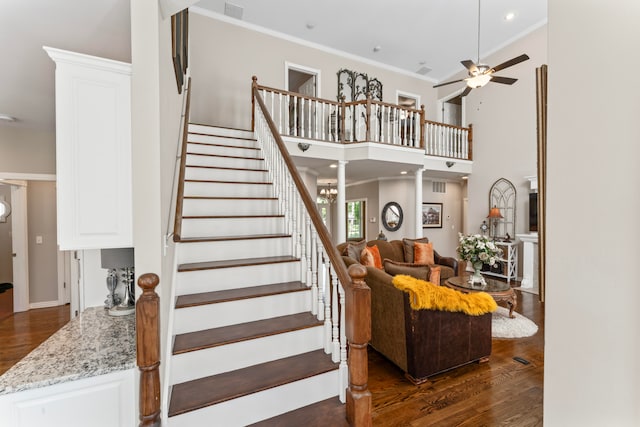 stairway with a towering ceiling, ornamental molding, hardwood / wood-style flooring, and ceiling fan