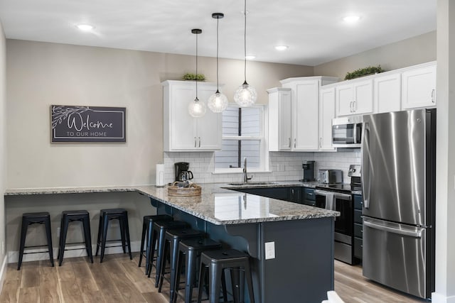 kitchen featuring stainless steel appliances, white cabinets, sink, kitchen peninsula, and hanging light fixtures