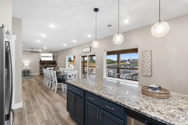 kitchen featuring stainless steel refrigerator, ceiling fan, light hardwood / wood-style flooring, decorative light fixtures, and a fireplace