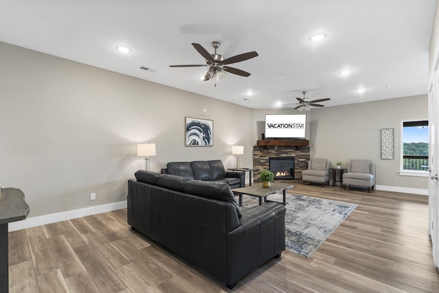 living room featuring ceiling fan, a stone fireplace, and wood-type flooring