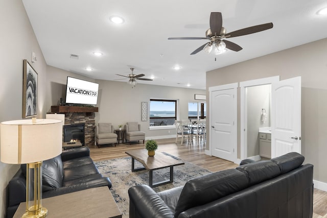 living room featuring light wood-type flooring, ceiling fan, and a stone fireplace