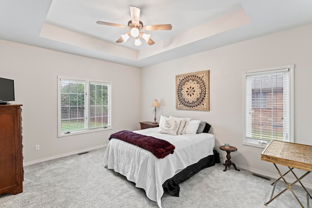 bedroom featuring multiple windows, ceiling fan, and a raised ceiling