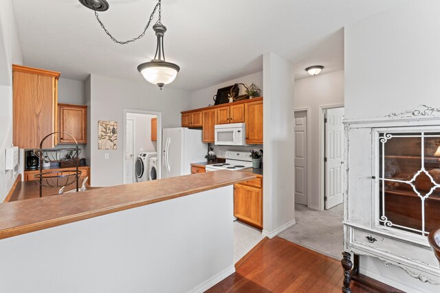 kitchen featuring white appliances, light hardwood / wood-style floors, decorative light fixtures, and separate washer and dryer