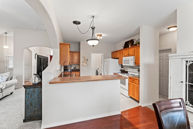 kitchen featuring separate washer and dryer, white appliances, kitchen peninsula, light hardwood / wood-style flooring, and decorative light fixtures