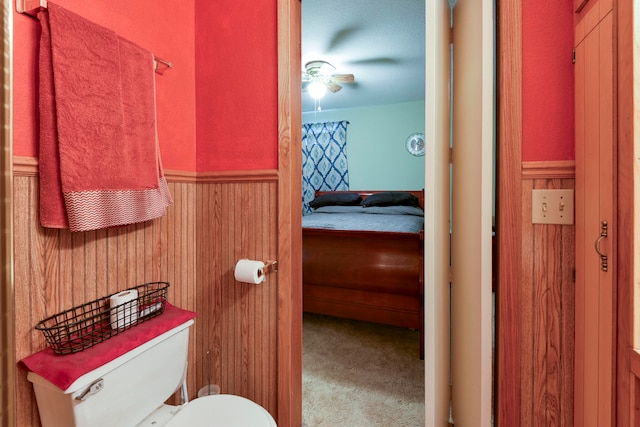 bathroom featuring ceiling fan, wood walls, and toilet