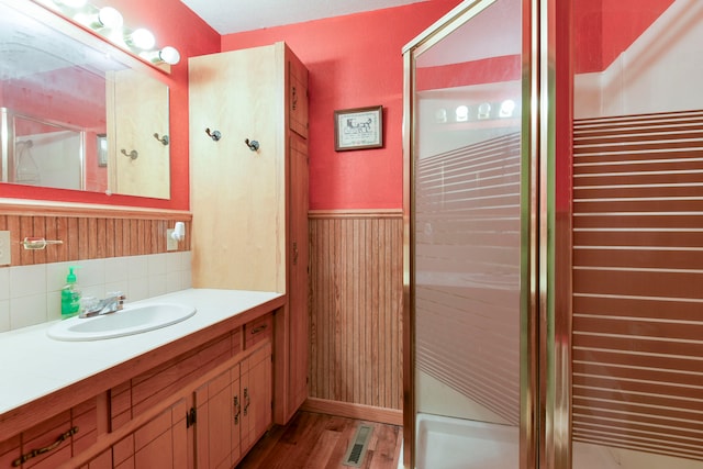 bathroom with walk in shower, wooden walls, hardwood / wood-style floors, and vanity