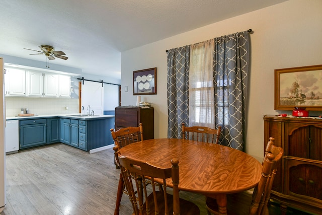 dining room featuring a healthy amount of sunlight, ceiling fan, a barn door, and light hardwood / wood-style flooring