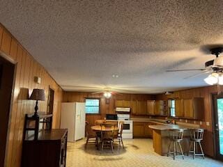 kitchen featuring light colored carpet, wooden walls, white appliances, and a textured ceiling