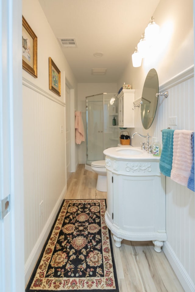 bathroom with wood-type flooring, a shower with shower door, vanity, and toilet