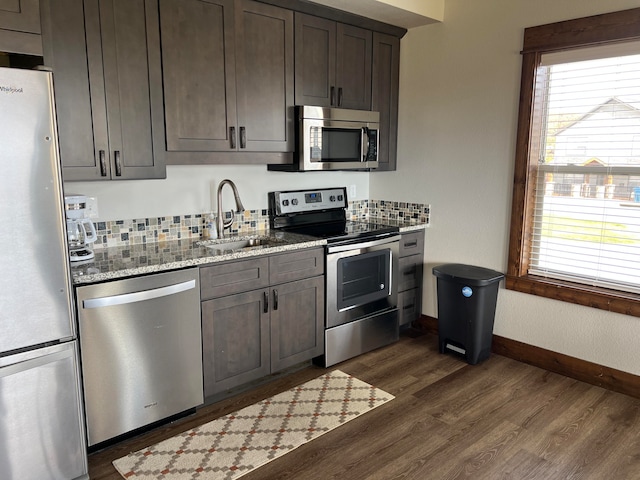 kitchen with dark brown cabinetry, sink, dark wood-type flooring, appliances with stainless steel finishes, and light stone countertops