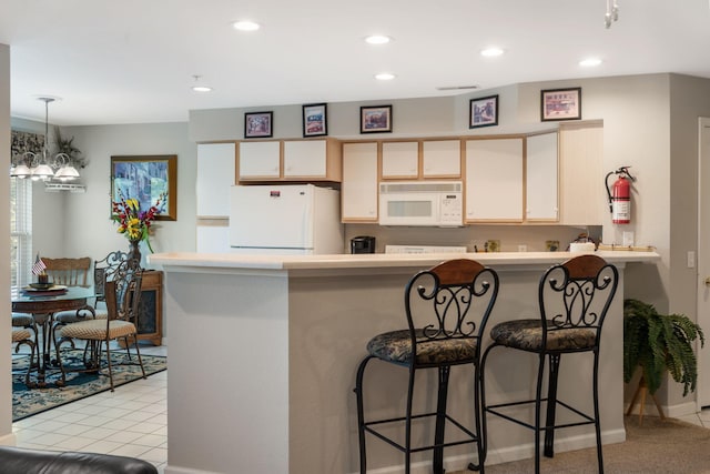 kitchen with a breakfast bar, white appliances, kitchen peninsula, a notable chandelier, and light colored carpet