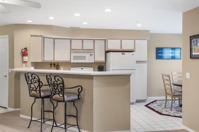 kitchen with ceiling fan, white appliances, kitchen peninsula, white cabinetry, and a kitchen bar