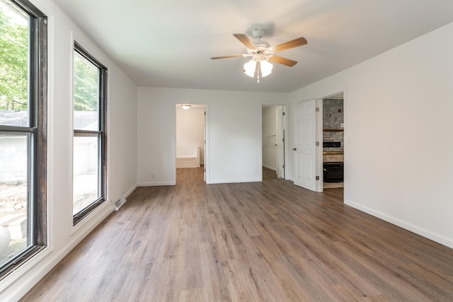 unfurnished bedroom featuring wood-type flooring, ceiling fan, a spacious closet, and ensuite bath