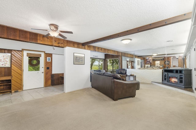 living room with ceiling fan, light colored carpet, beam ceiling, wooden walls, and a textured ceiling