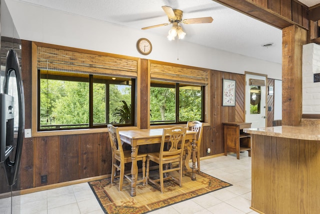 tiled dining area with wood walls, plenty of natural light, ceiling fan, and a textured ceiling