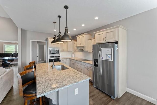 kitchen with sink, light stone countertops, an island with sink, appliances with stainless steel finishes, and a kitchen bar