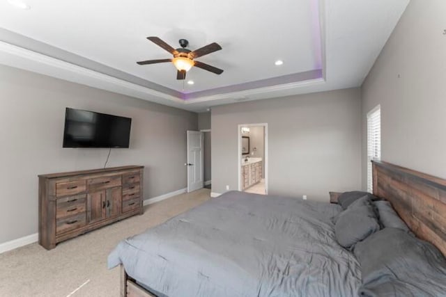 bedroom featuring ceiling fan, a tray ceiling, connected bathroom, and light colored carpet