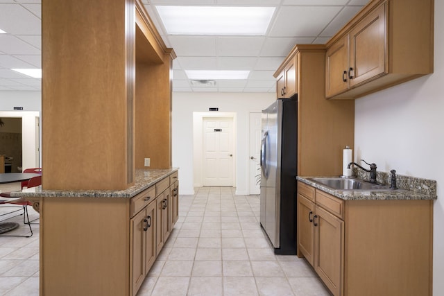 kitchen featuring a drop ceiling, stainless steel refrigerator, sink, and a breakfast bar area