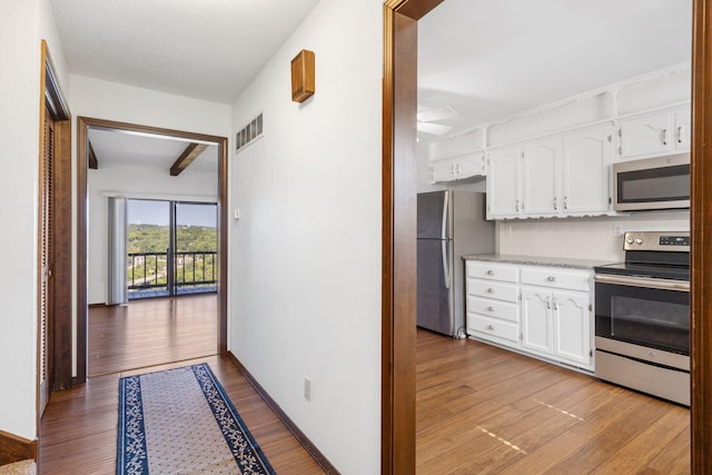 kitchen with stainless steel appliances, white cabinets, light hardwood / wood-style flooring, beam ceiling, and a textured ceiling