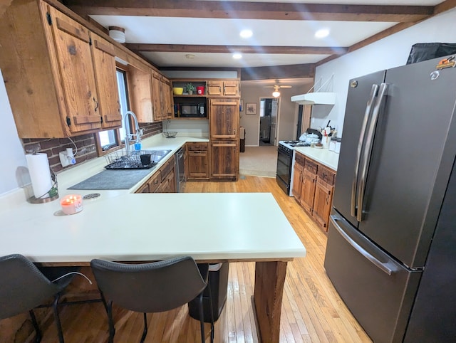 kitchen with black appliances, a kitchen breakfast bar, sink, light wood-type flooring, and kitchen peninsula